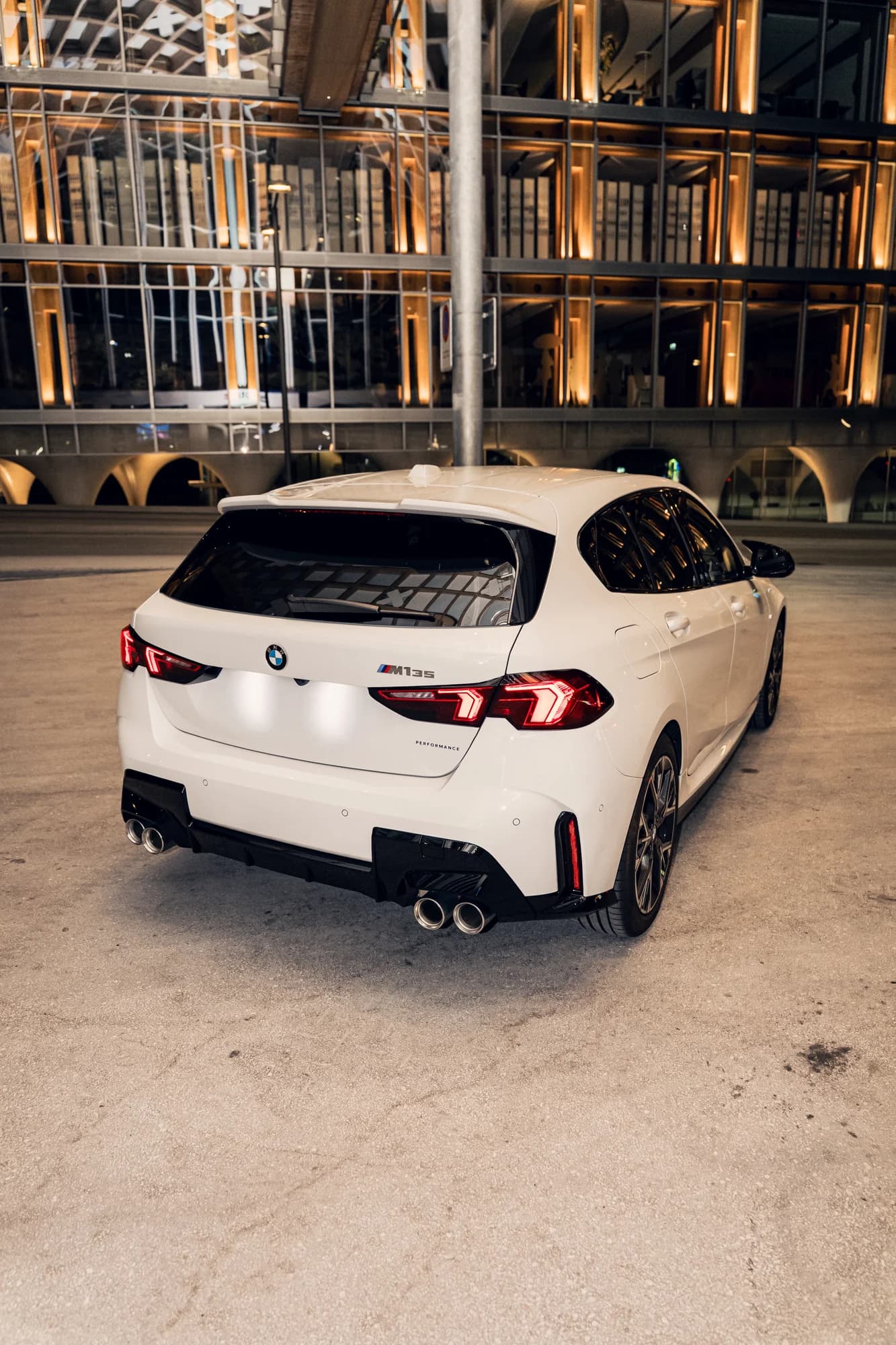 Arrière de la BMW M135 blanche devant une façade illuminée